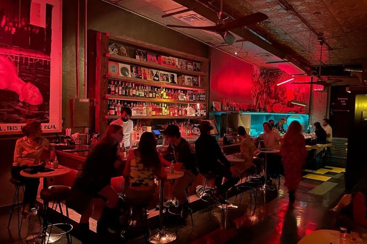 The bar, lit red, with record sleeves on the back shelf and guests on stools