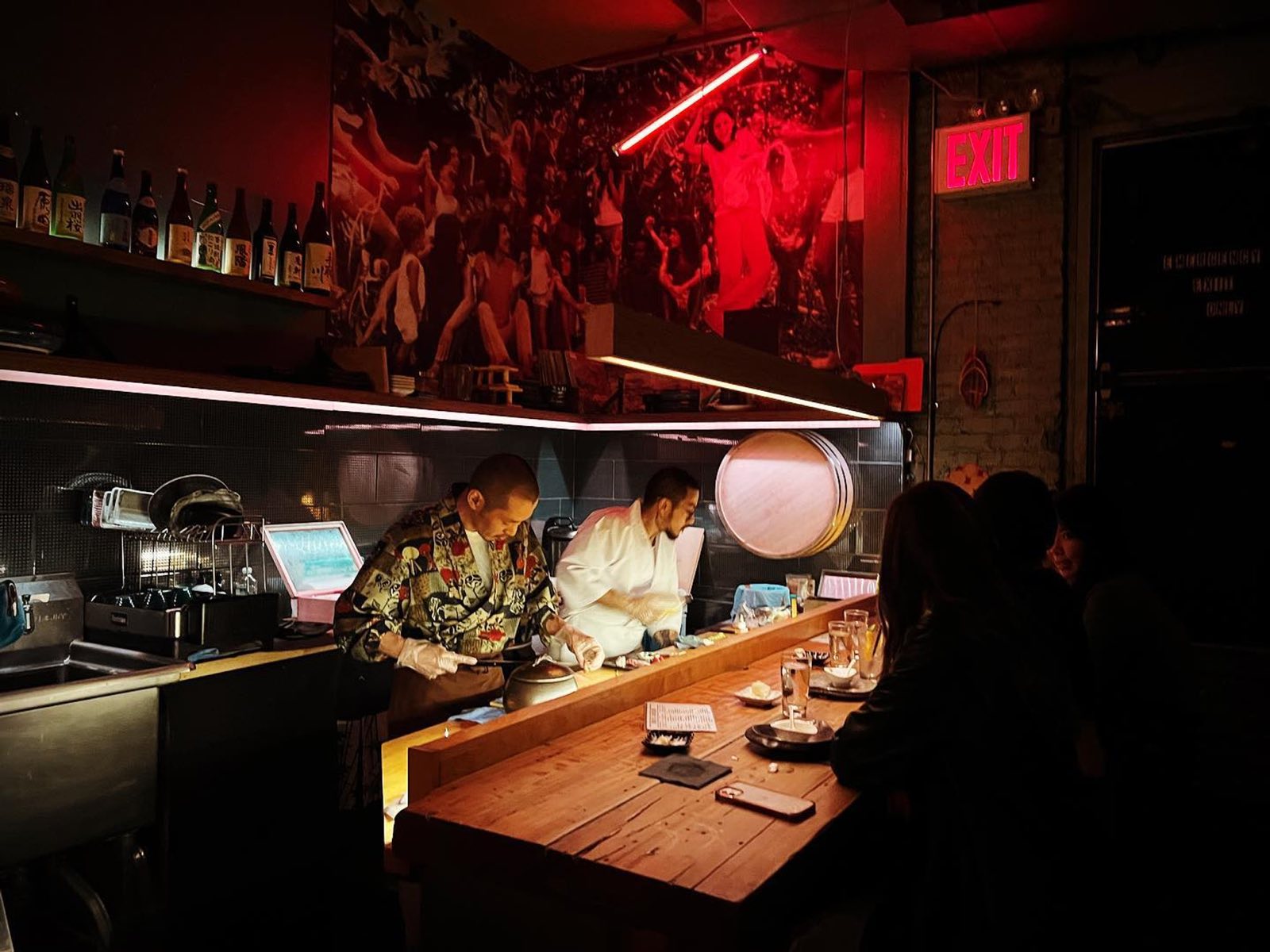Two chefs at the sushi bar under a red neon tube