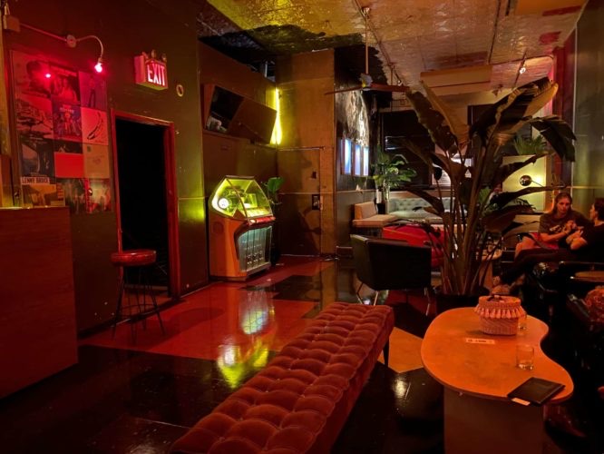 A lit jukebox beside a velvet bench and plants